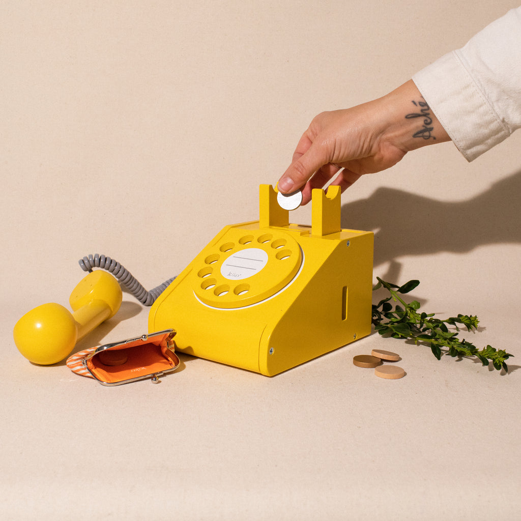 hand dropping coin into yellow wooden rotary phone with coin purse and extra coins