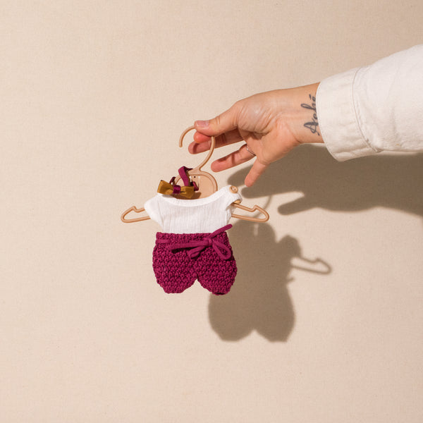hand holding Miniland white and burgundy short set on hanger 