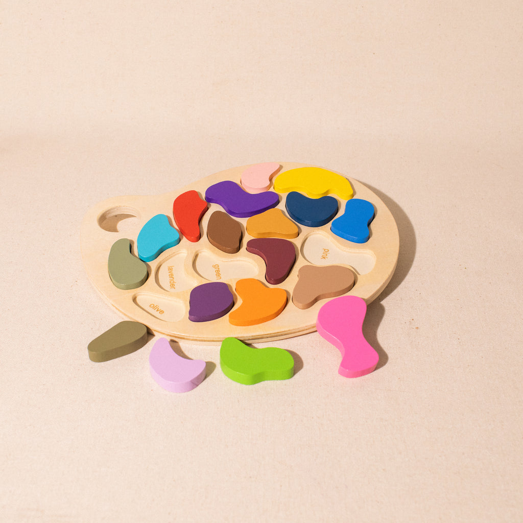 wooden artist palette puzzle with some coloured shapes removed showing name of colour underneath
