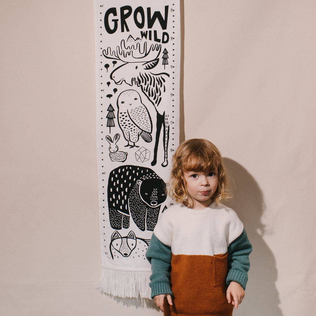 child standing beside canvas growth chart illustrated with black and white woodland animals